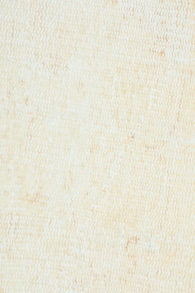 Macro shot of the low wool pile, showing the hand-knotted texture and soft cream color.
