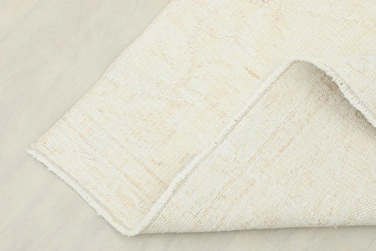Corner of the rug folded back, showing the backside of the hand-knotted wool pile and cotton foundation.