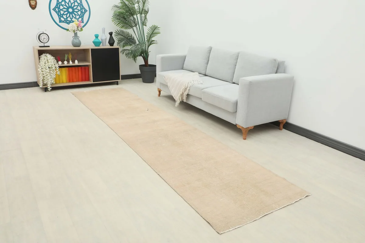 Muted tan runner rug laid in a room with a light gray sofa and wooden cabinet, showing its scale.