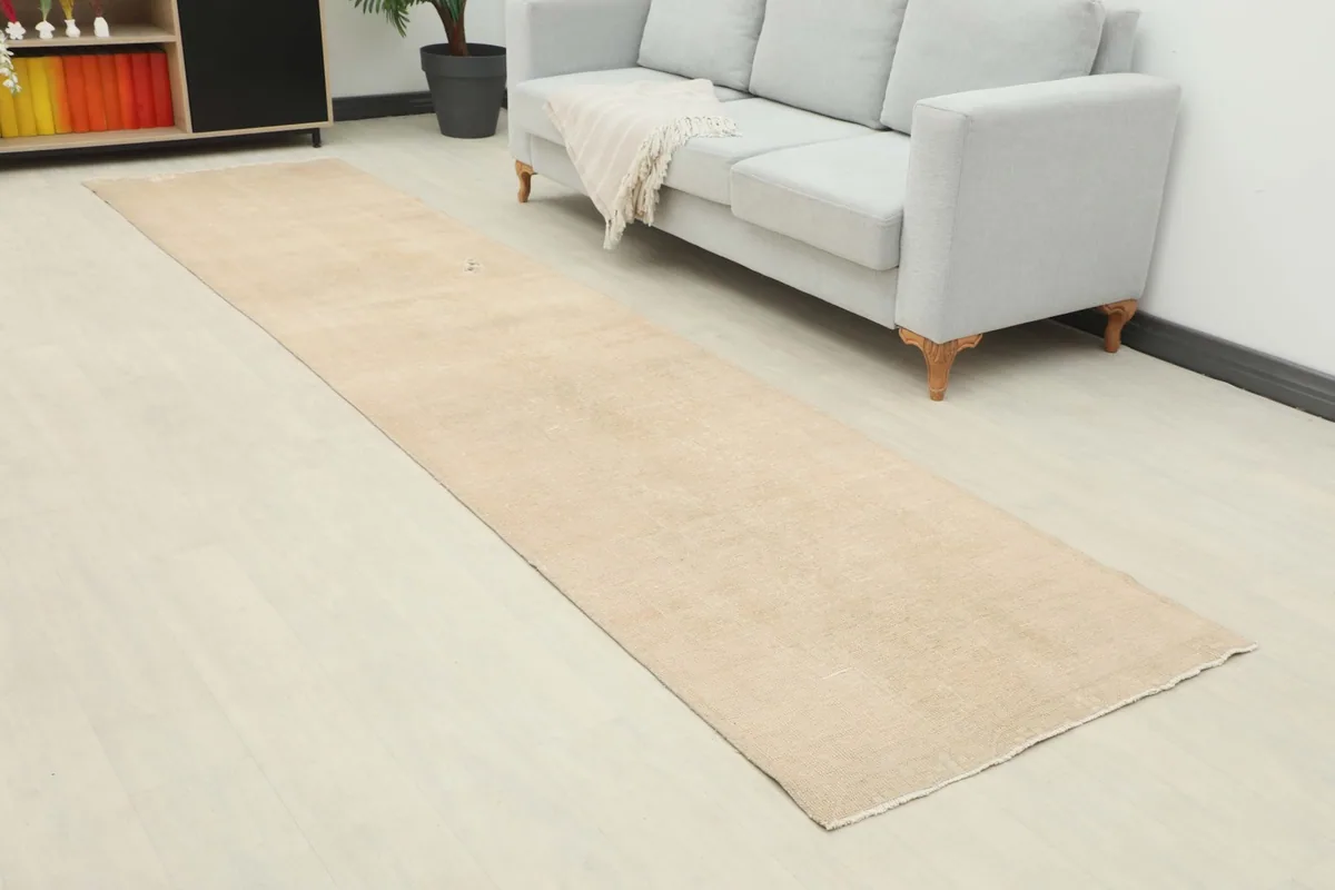 Angled view of the long tan runner rug in a room setting, beside a sofa and cabinet.