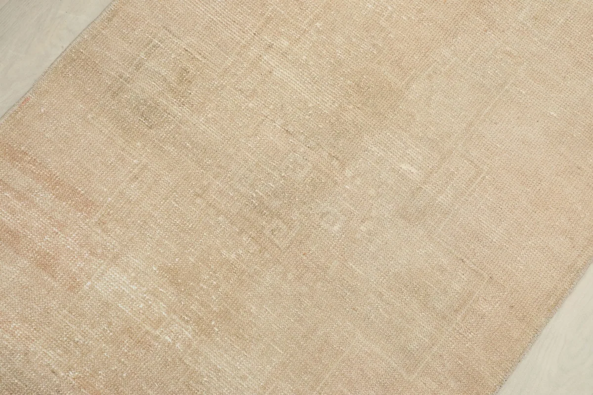 Overhead detail showing faint geometric patterns within the muted tan wool pile.