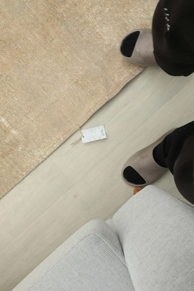 Overhead view of a small tag on the floor next to the runner rug, near a person's feet