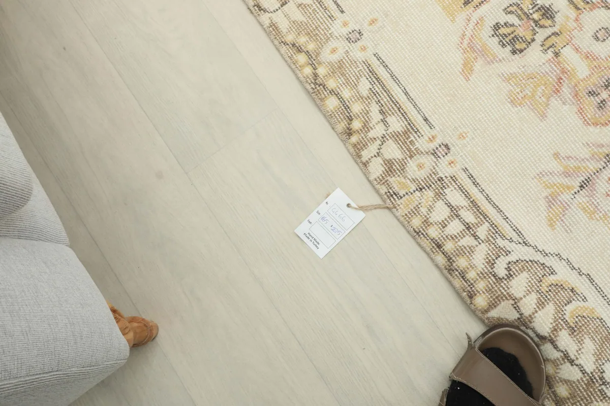 Top-down view showing the size tag attached to the rug's edge next to a foot, providing scale.