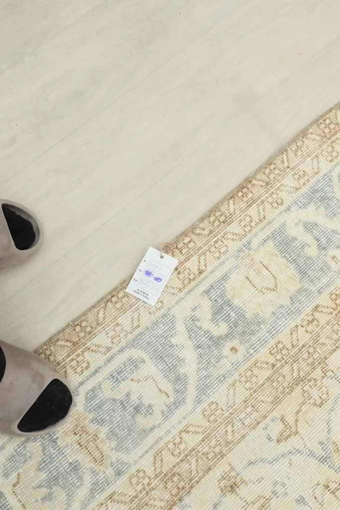 View of the rug's edge with a size tag, next to feet for scale reference