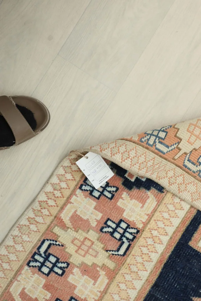 Close-up of the rug's corner with an informational tag, next to a shoe for scale.