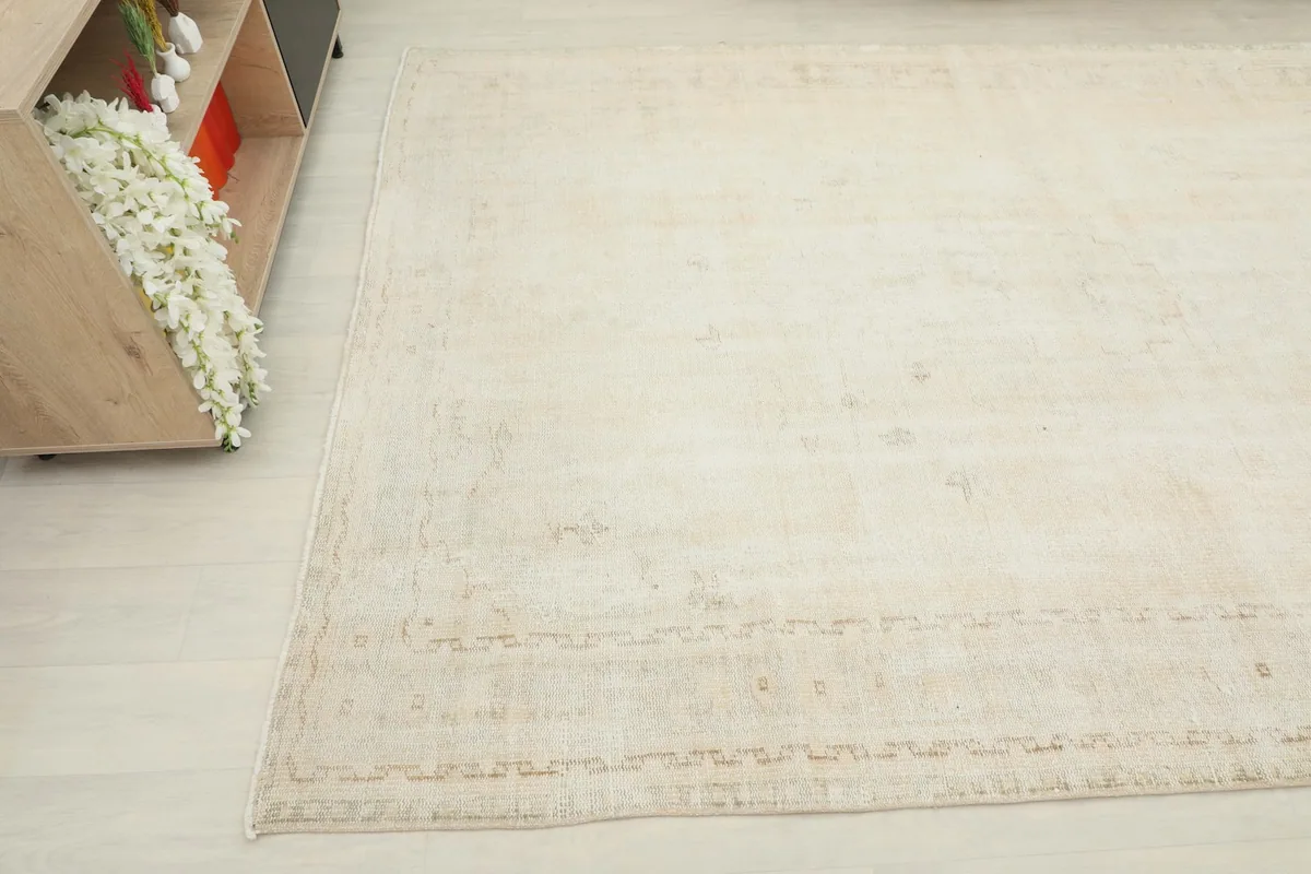 Close-up angled view showing the texture and faded beige patterns near the border of the ivory rug.
