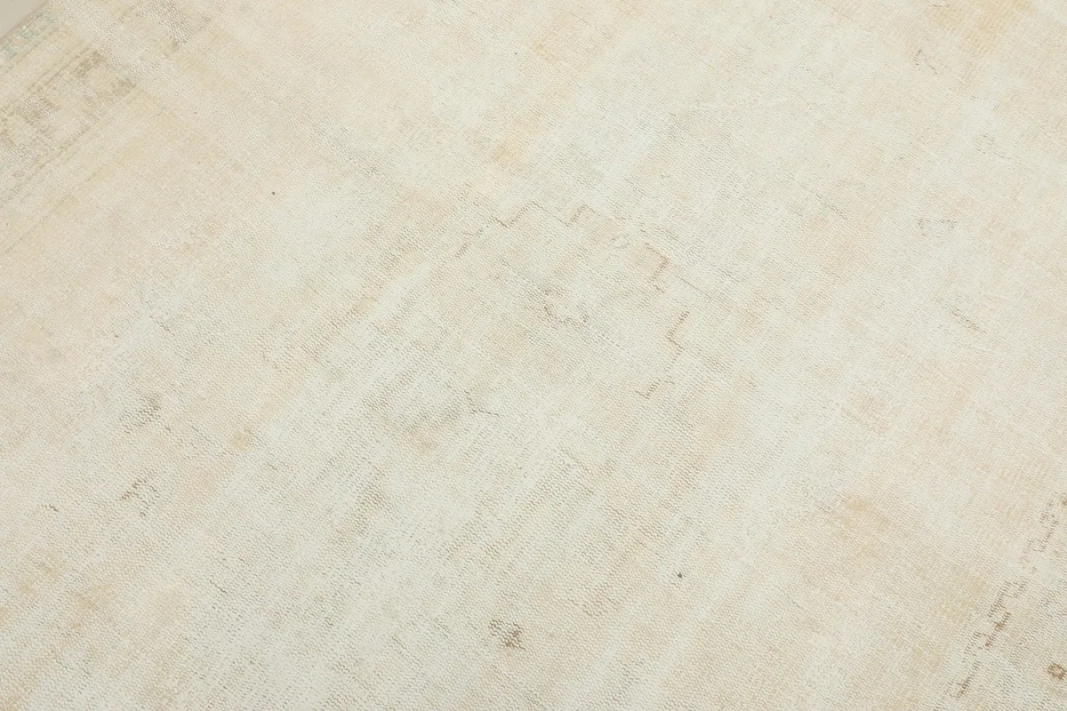 Detailed view of the ivory rug's low pile and the very faint, distressed geometric design in the field.