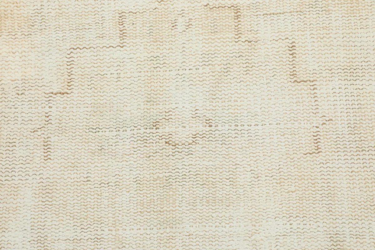 Close-up of a central motif on the ivory rug, showing the hand-knotted wool texture and faded beige lines.