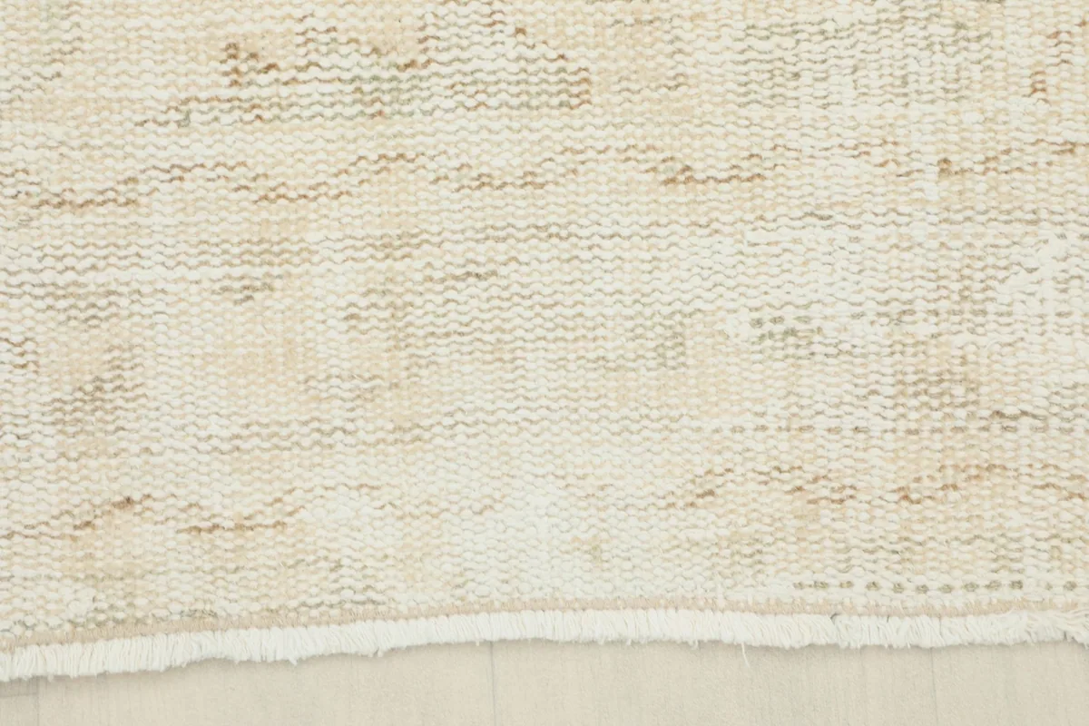 Edge of the ivory rug, showing the short, natural fringe and the subtle border pattern.