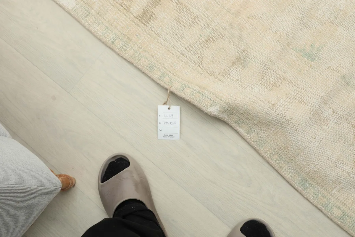 View from above showing a tag attached to the rug's edge, alongside a person's feet for scale.