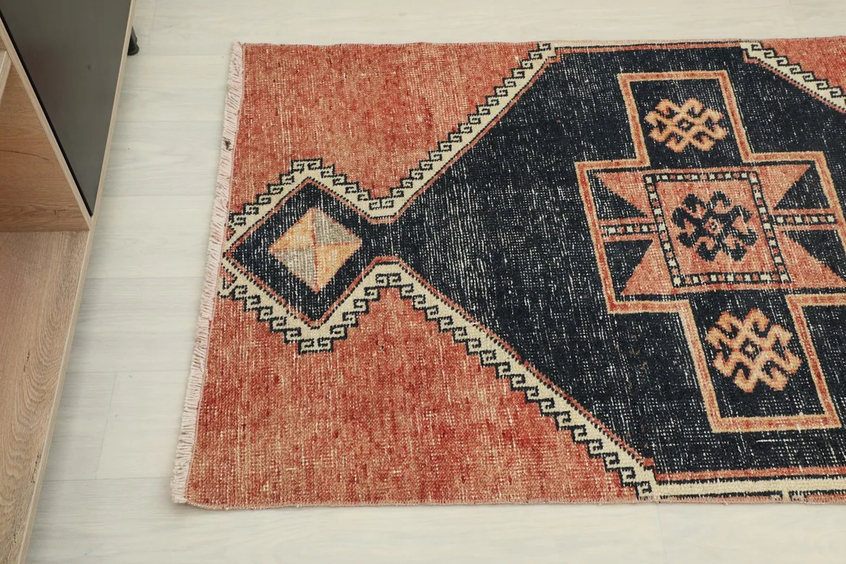 Angle view of the vintage runner rug's end, highlighting the rust main field and navy patterns