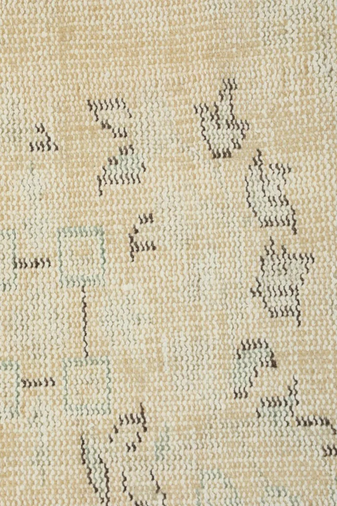 Extreme close-up of the low wool pile and hand-knotted texture with faded gray threads