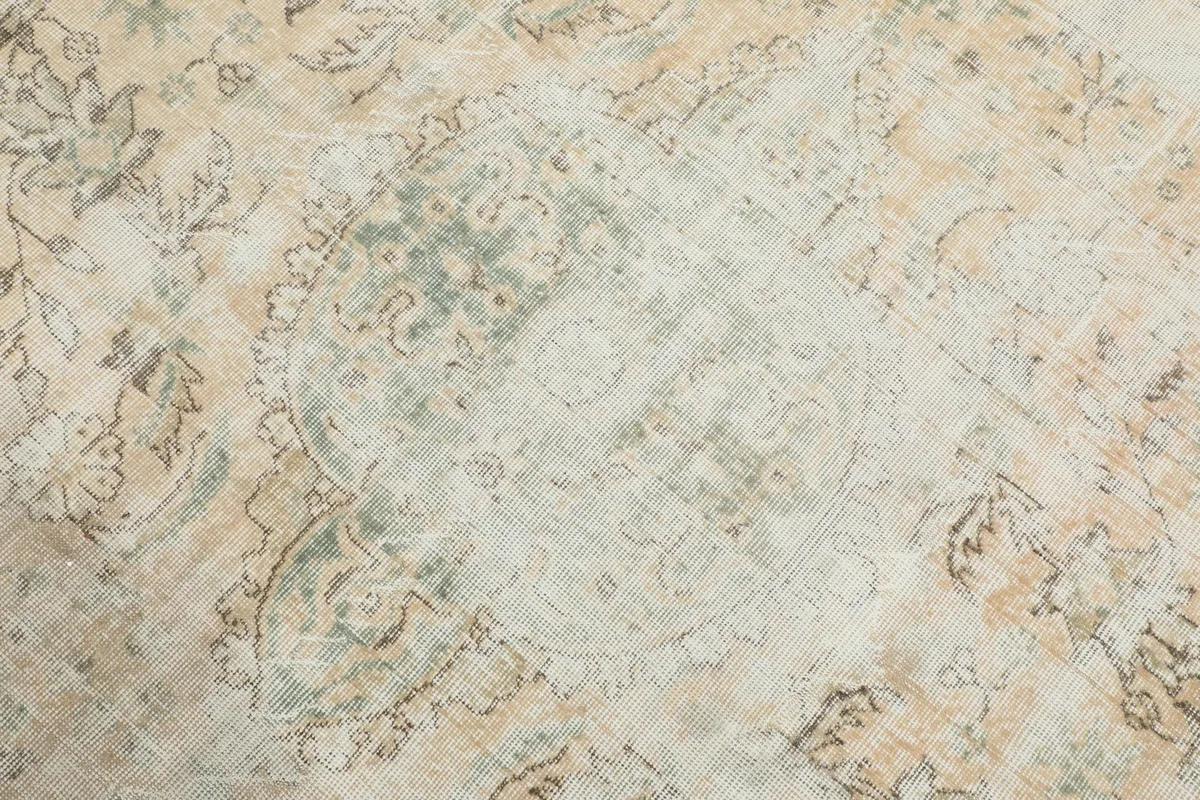 Detailed view of the central medallion and surrounding faded motifs, showing the blend of ivory, beige, and green tones.