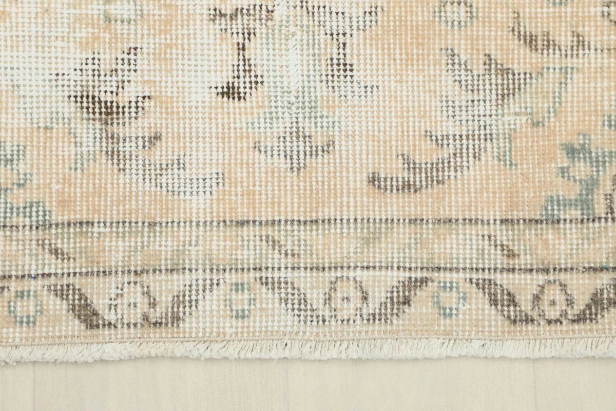 Detail of the rug's border and fringe, showing the muted colors and the worn edge characteristic of vintage pieces.