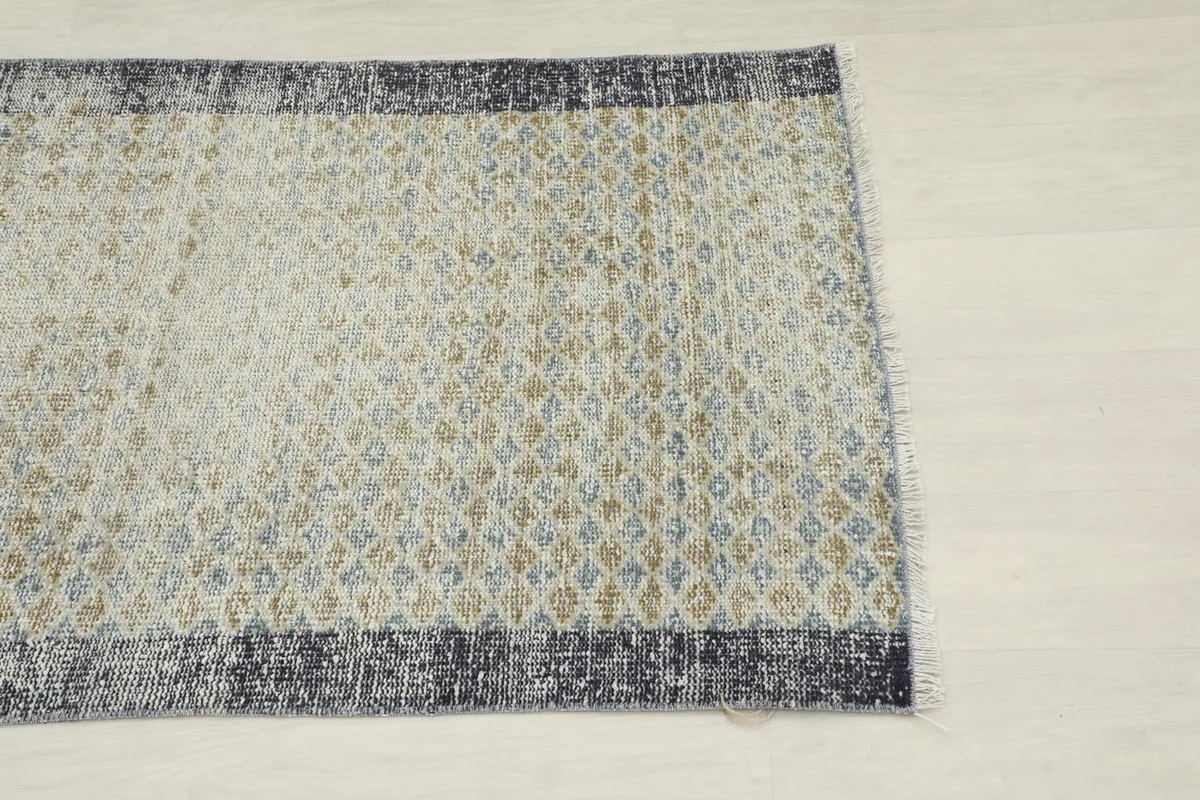 Overhead view of one end of the rug, showing the ivory field with blue and tan diamond motifs and the border.