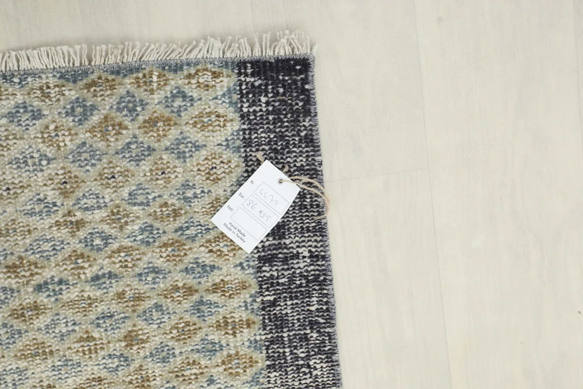 Corner of the rug with a product tag, displaying the hand-knotted construction and distressed border detail.