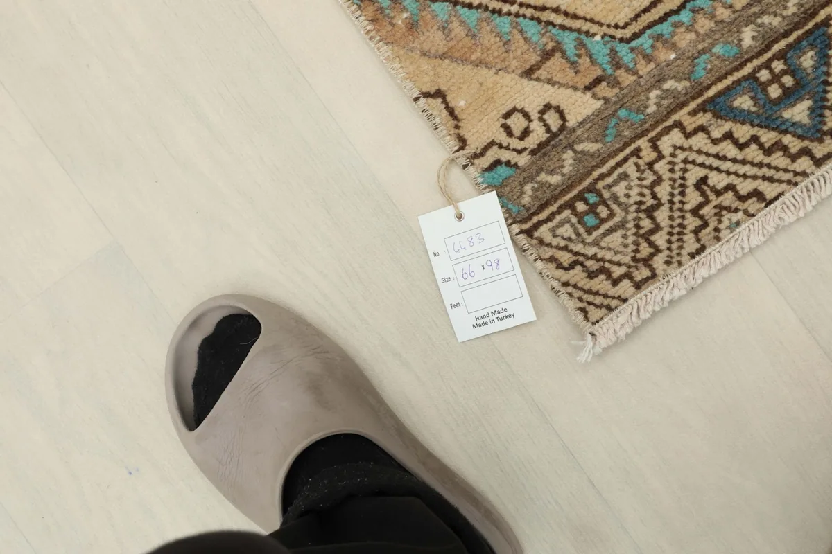 A foot next to the rug with a tag, showing the rug's relative size and scale on a light floor.