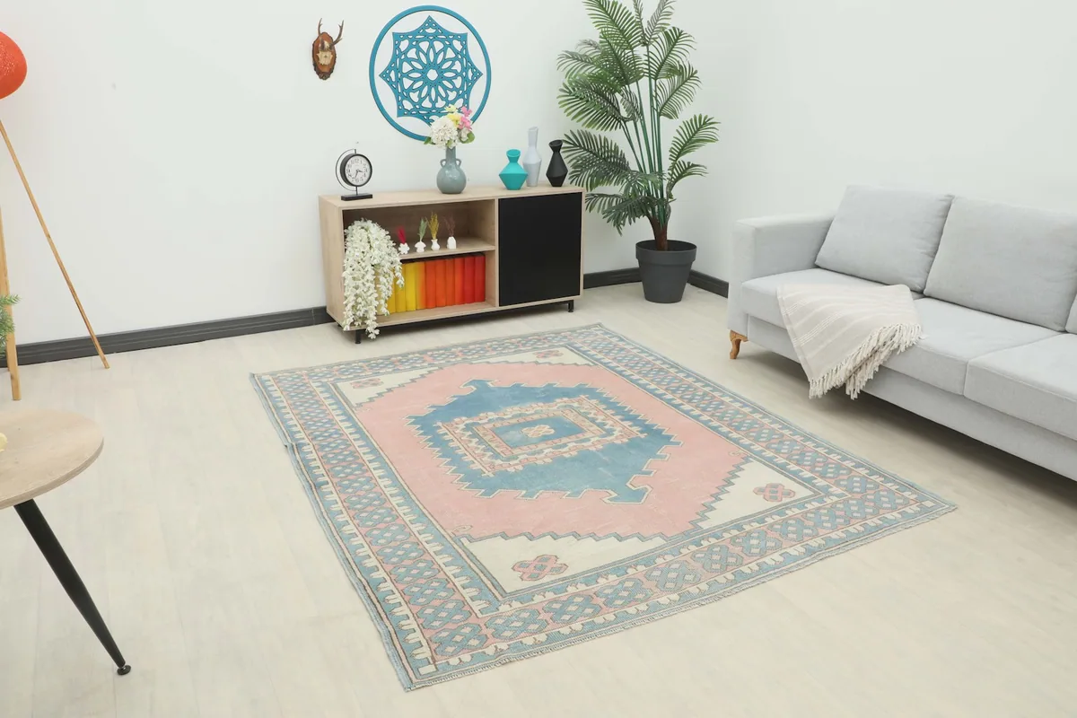 Vintage pink and blue Anatolian rug displayed in a bright living room setting with a sofa and cabinet