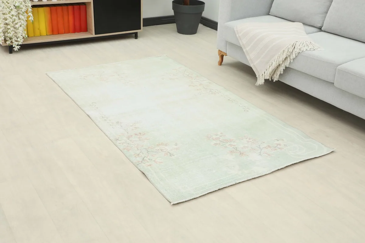 Angle view of the rose green rug in a room, showing its placement in front of a sofa