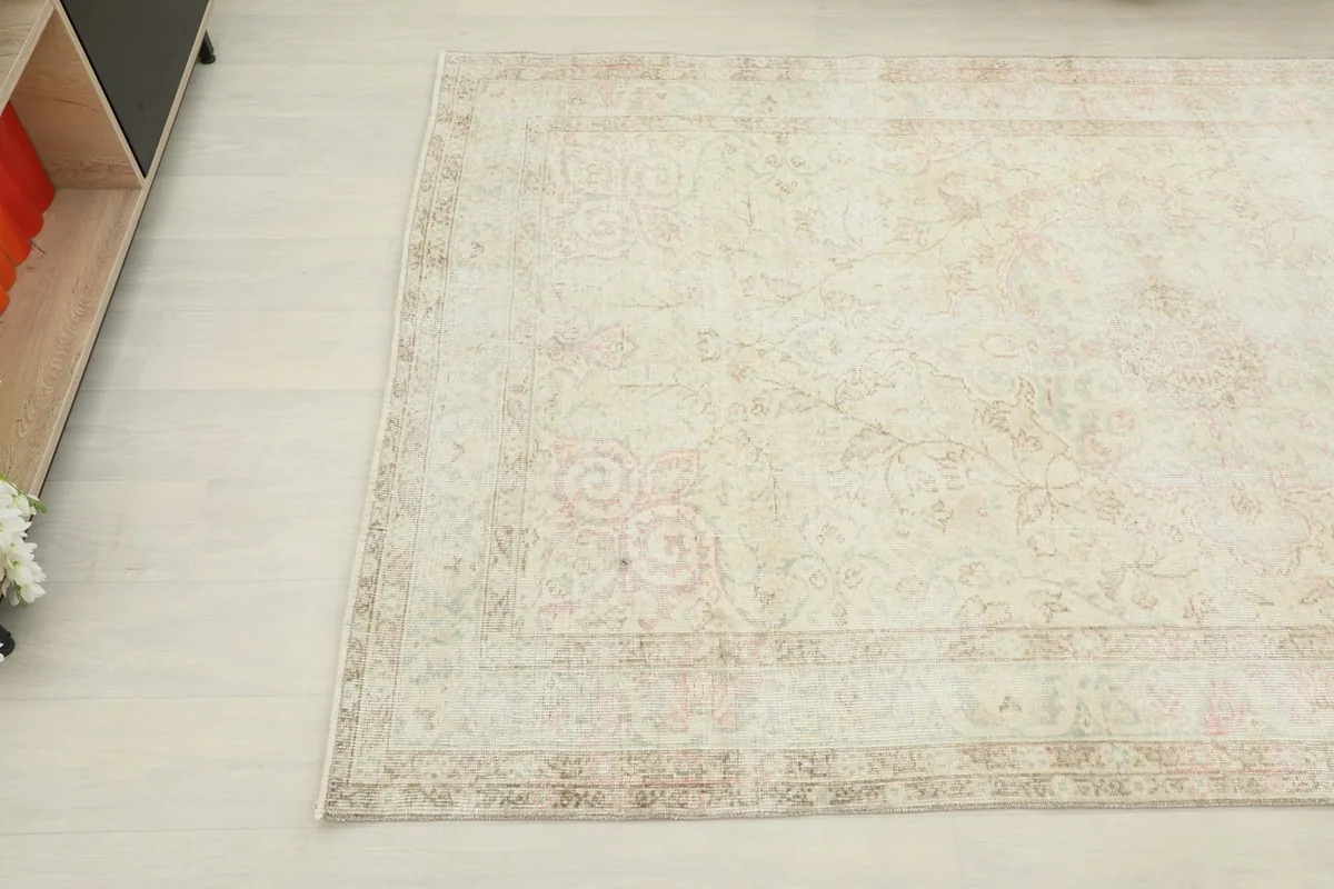 Top-down angled view of the rug, emphasizing the soft ivory field and worn patterns