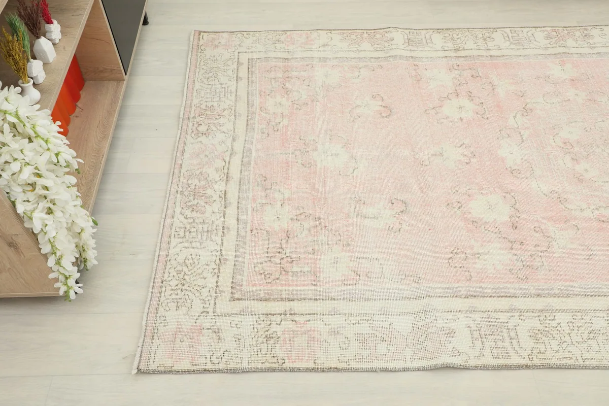 Corner view of the vintage rug showing the rose field, cream border, and subtle signs of wear