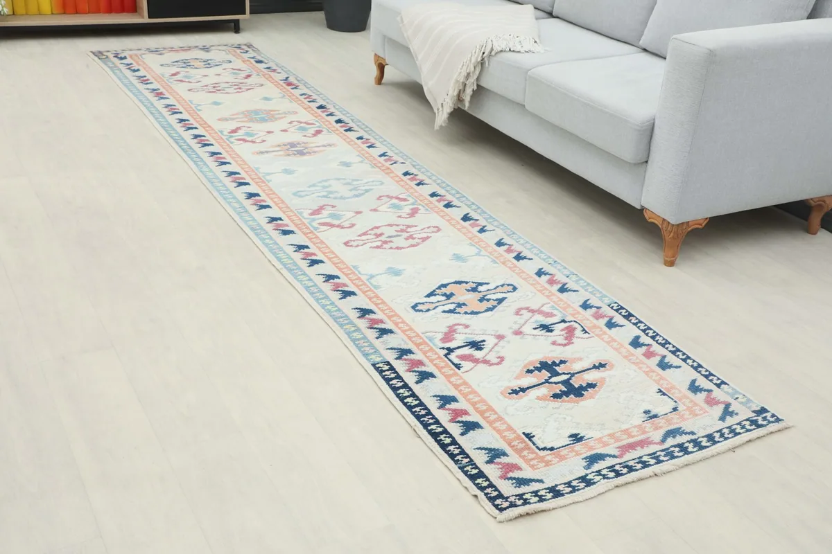 Angled view of the cream runner rug on a light floor, showing its length next to a gray sofa.