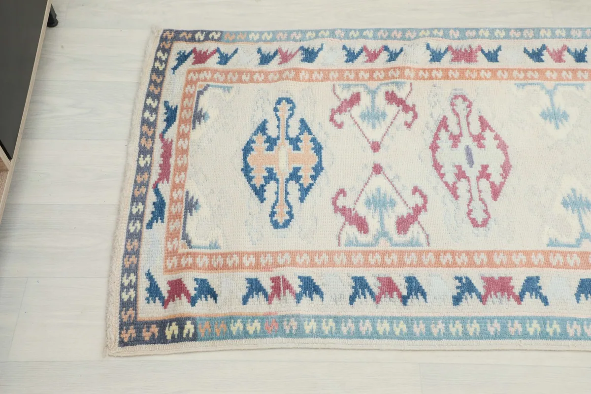 Detail view of the rug's patterns and border, highlighting the blue, rose, and tan colors.