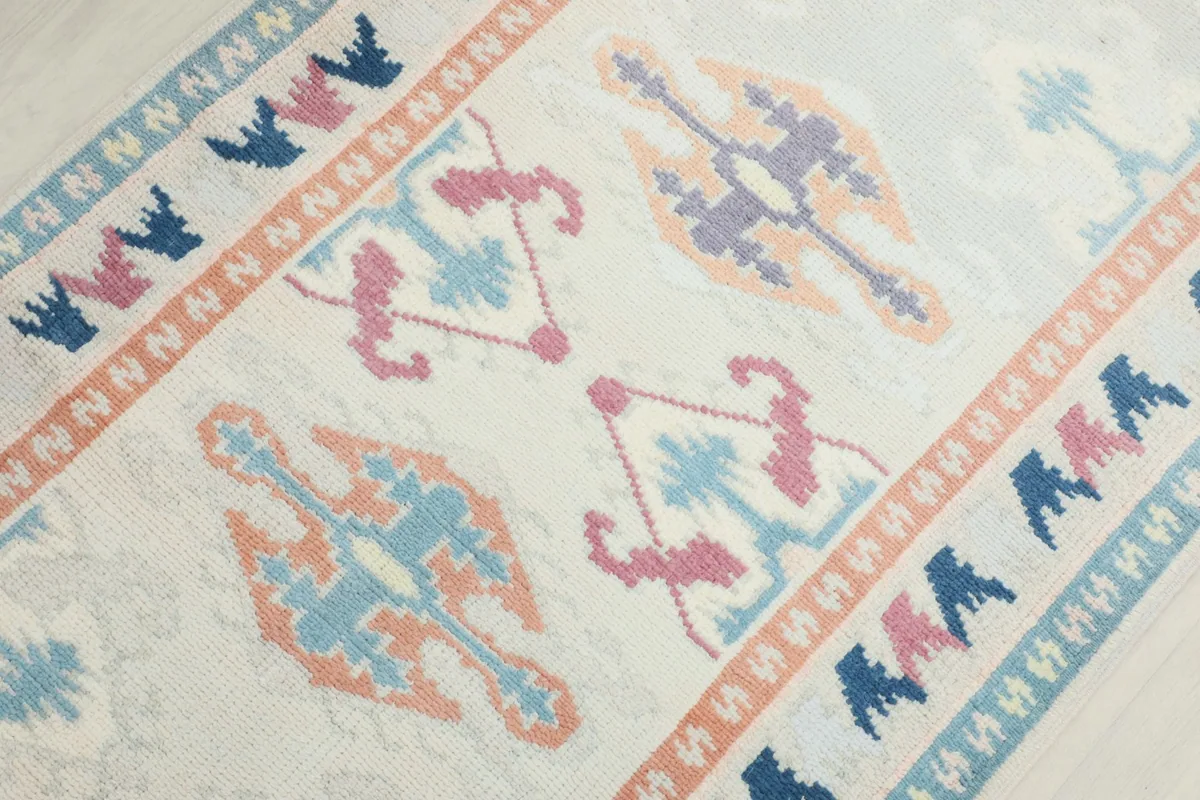 Overhead close-up of the rug's central design, featuring various blue, rose, and tan tribal shapes.