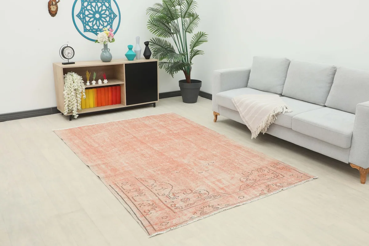 Vintage soft rose Anatolian rug placed in a modern living room setting with a light gray sofa and wooden cabinet.