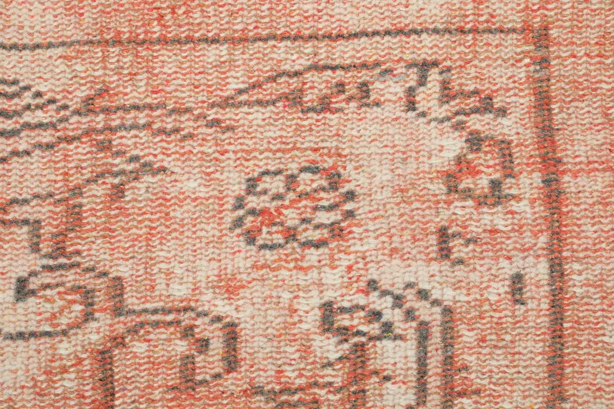 Detailed view of the hand-knotted wool pile, highlighting the subtle gray geometric motifs within the rose field.