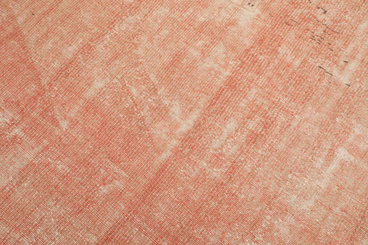 Close-up detail of the low wool pile, showing the soft rose color with natural wear and abrash.