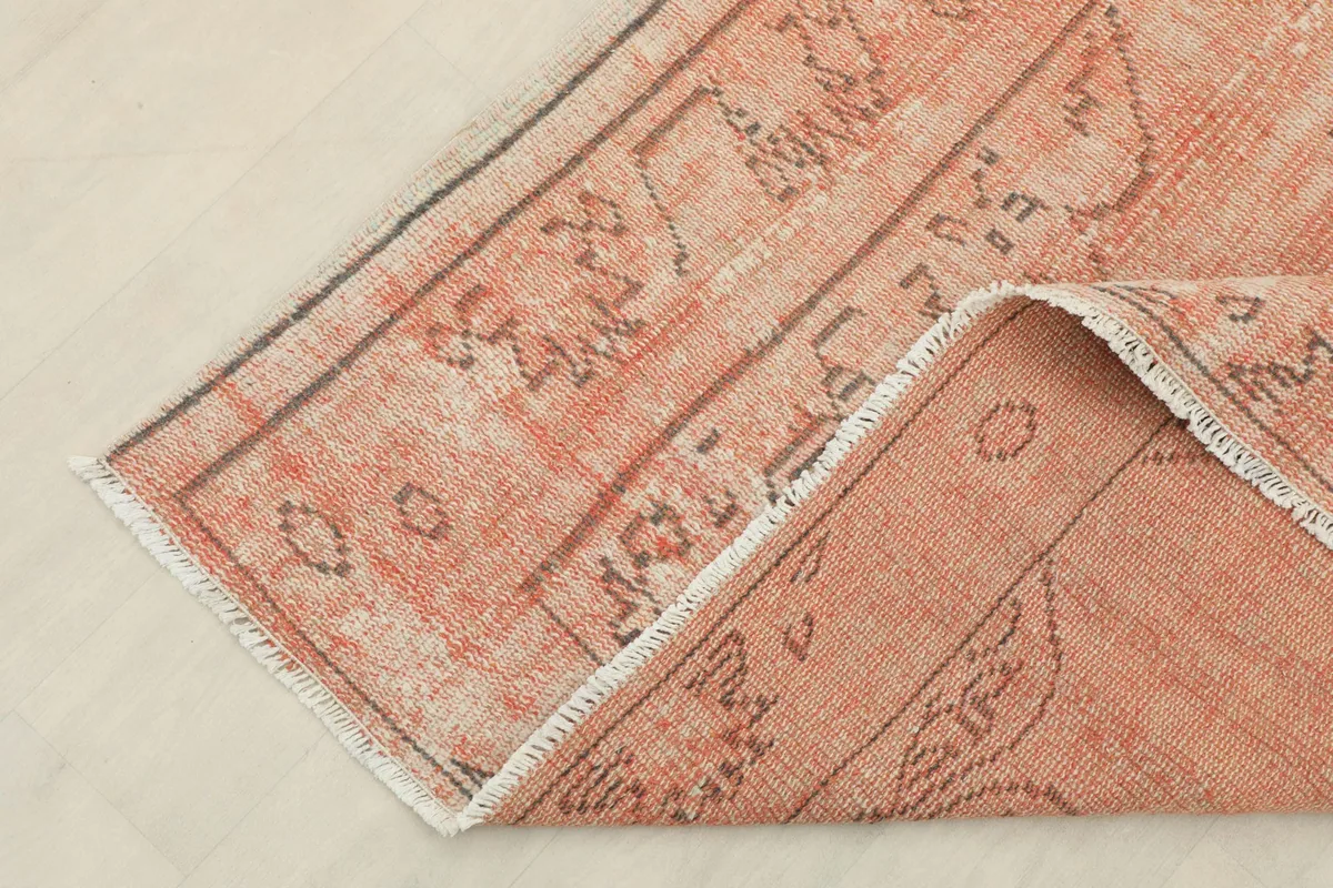 Folded corner of the rug, revealing the soft rose wool pile and the hand-knotted construction.