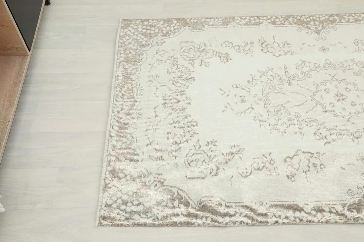 Overhead angle view highlighting the faded tan floral patterns and border on the ivory rug.