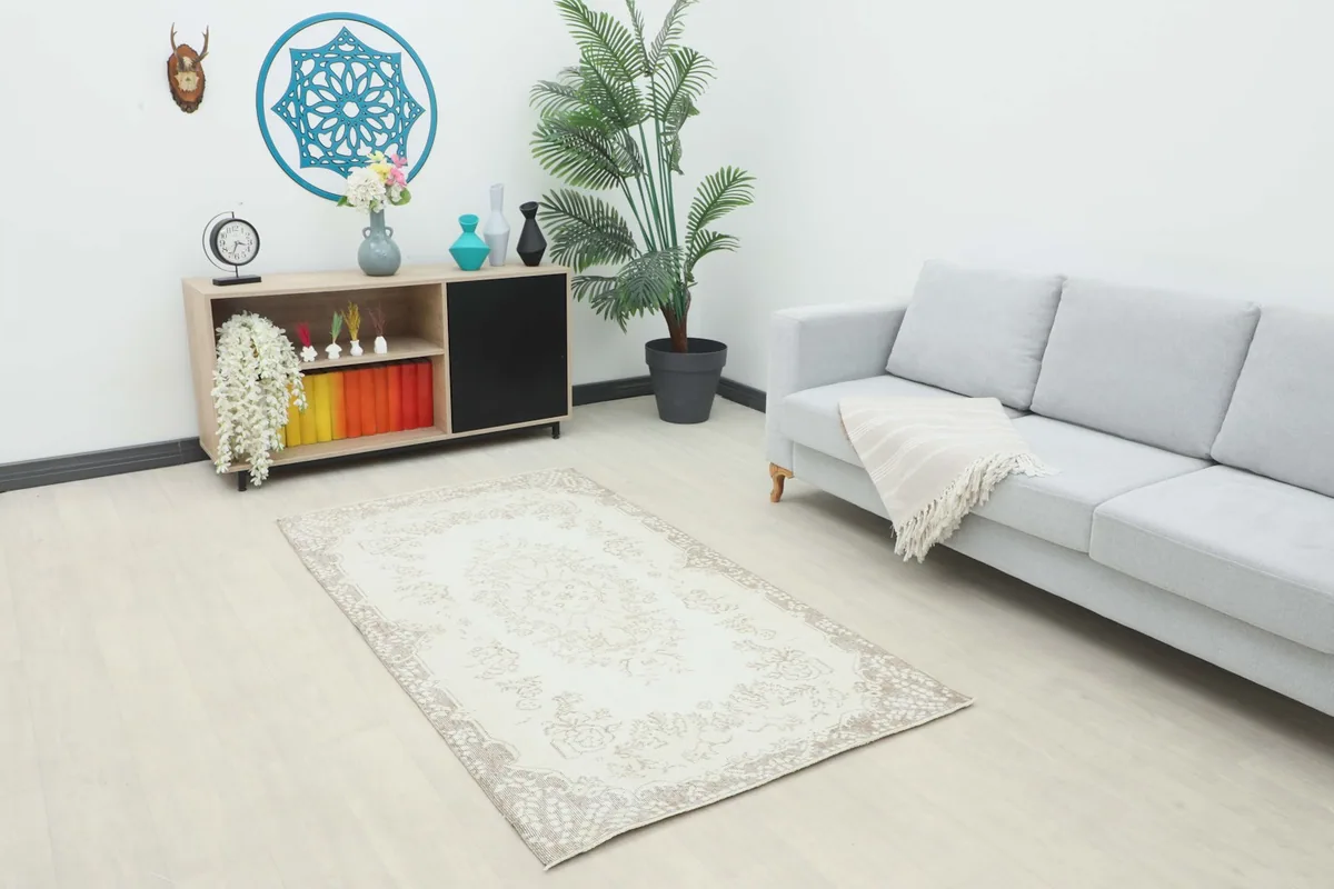 Ivory and tan rug in a living room setting with a sofa and cabinet, showing its scale.