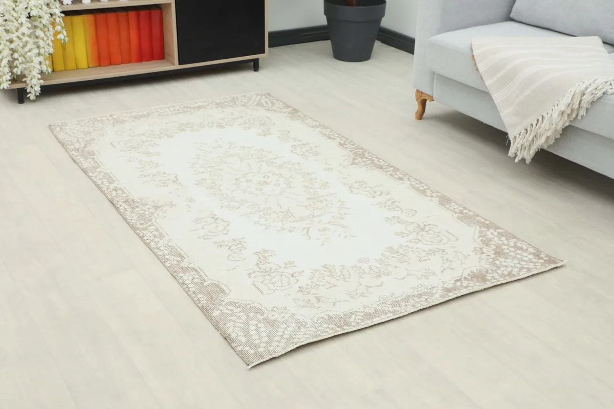 Angle view of the ivory and tan vintage rug on a light floor in a room setting.