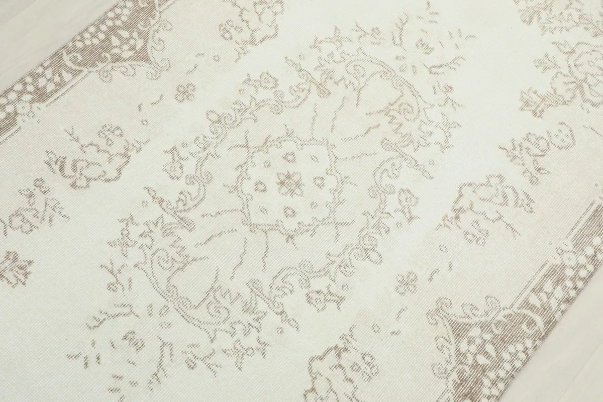 Detailed view of the central medallion and surrounding floral elements in muted tan on ivory.