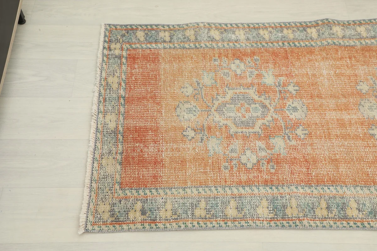 Angled view of the other end of the rust runner rug, showing the faded rust field and blue border.