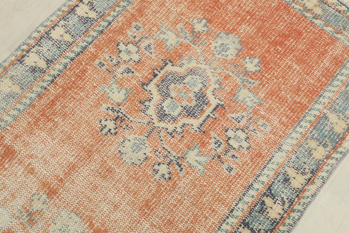 Detailed close-up of a central geometric design on the rust rug, featuring blue, gray, and cream colors.