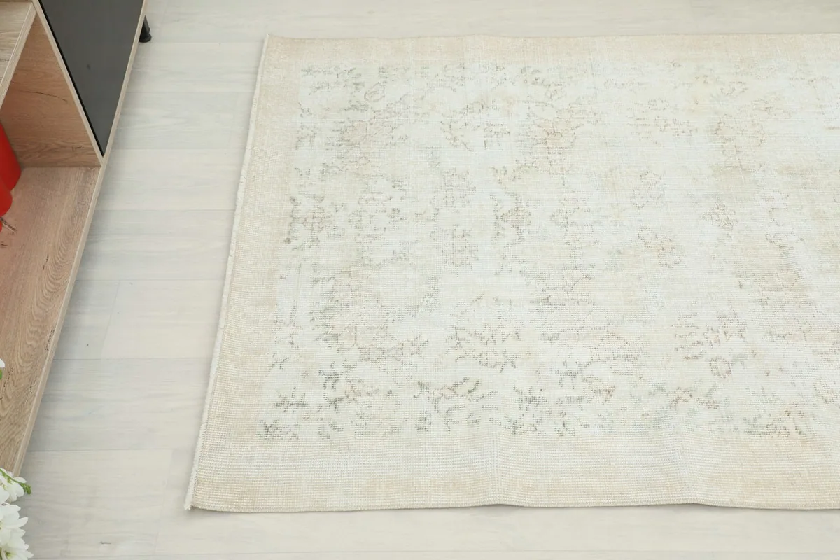 Close-up of the lower left corner of the cream rug with faint patterns near a cabinet