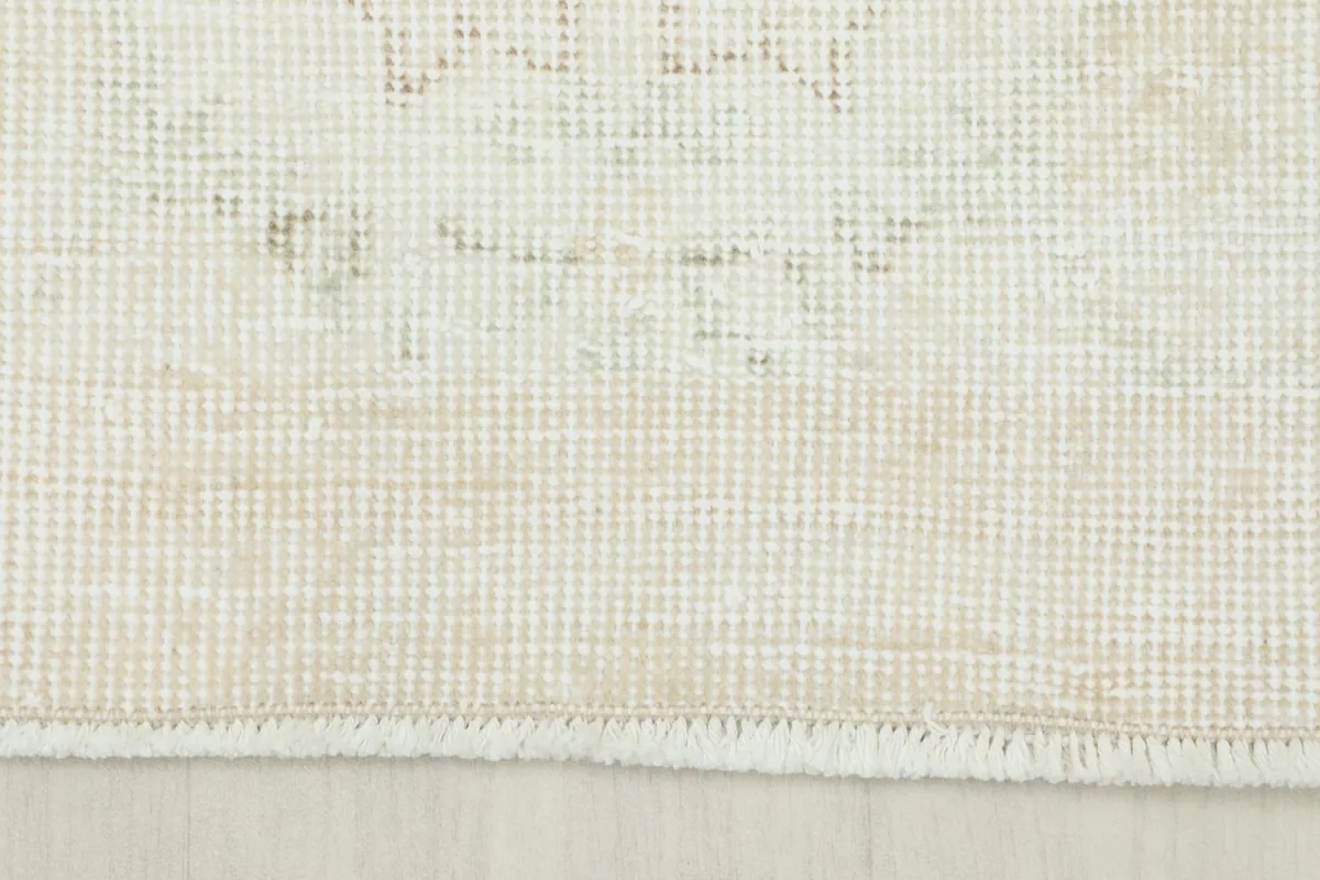 Close-up of the short, natural cotton fringe and the edge of the cream hand-knotted rug