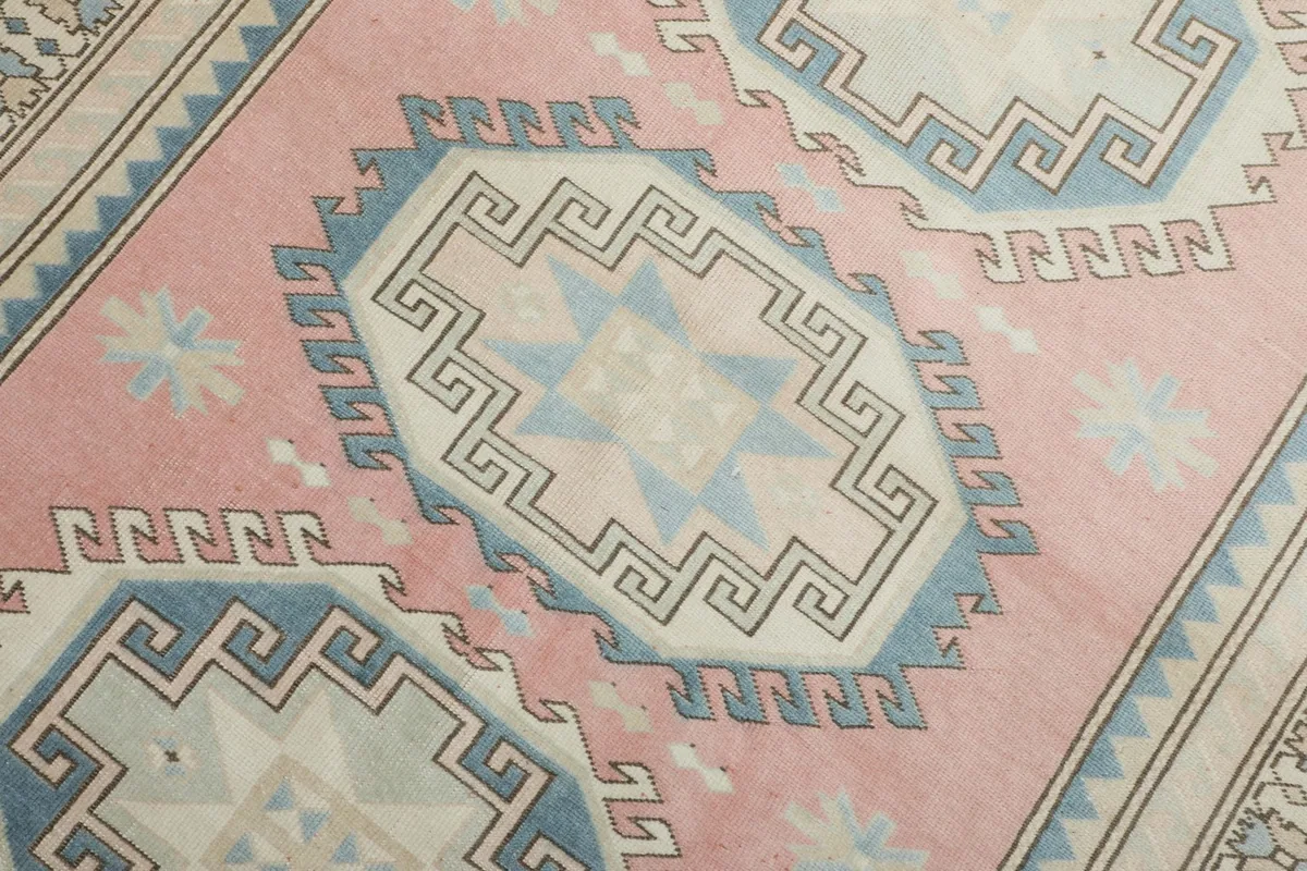 Detailed view of a central blue and ivory geometric medallion with intricate patterns on the pink field
