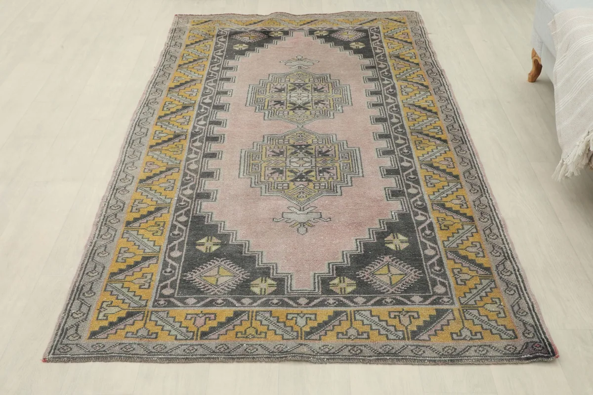 Overhead view of the entire rose, gold, and gray vintage Anatolian rug on a light floor