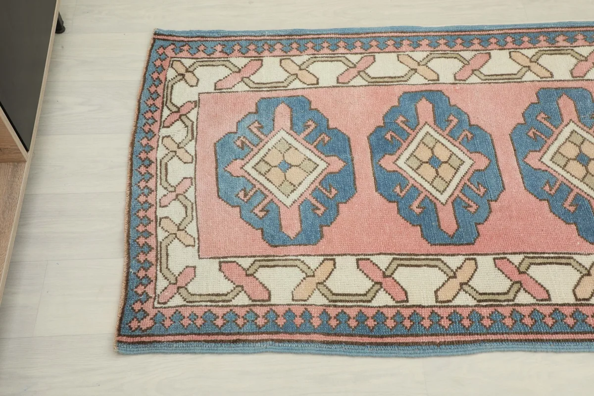Another angled view of the rug's pattern and border, showing the interplay of rose, blue, ivory, and tan colors.