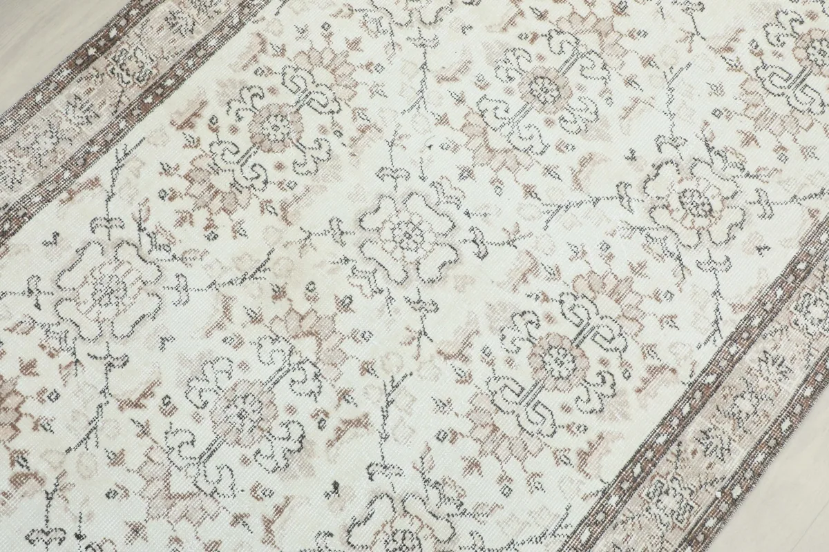 Detailed view of the repeating floral and vine motifs in gray and tan on the cream background