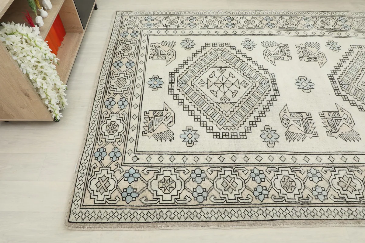 Detailed angle showing the ivory field, gray tribal motifs, and light blue floral accents near furniture.