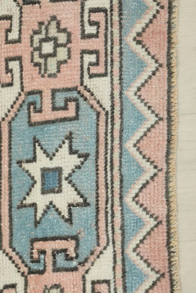 Close-up of the rug's border, showing the intricate blue and rose geometric patterns and low pile