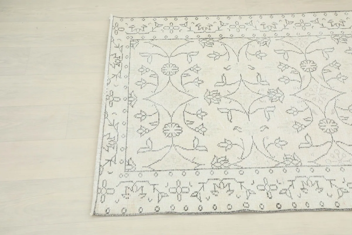 Corner view of the rug, showcasing the intricate gray motifs against the ivory field and border design.