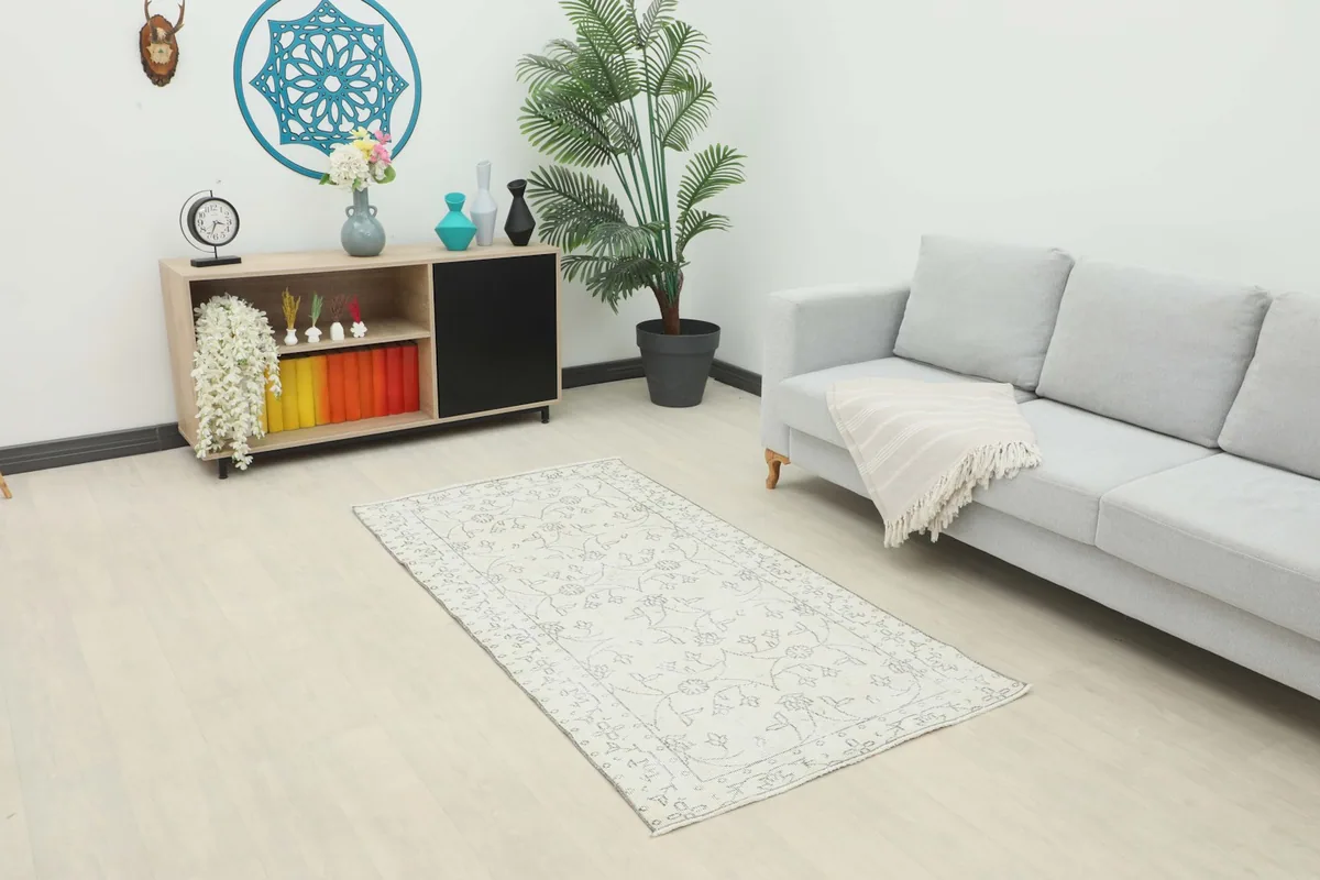 Ivory and gray area rug placed in a living room setting with a light gray sofa and wooden cabinet.