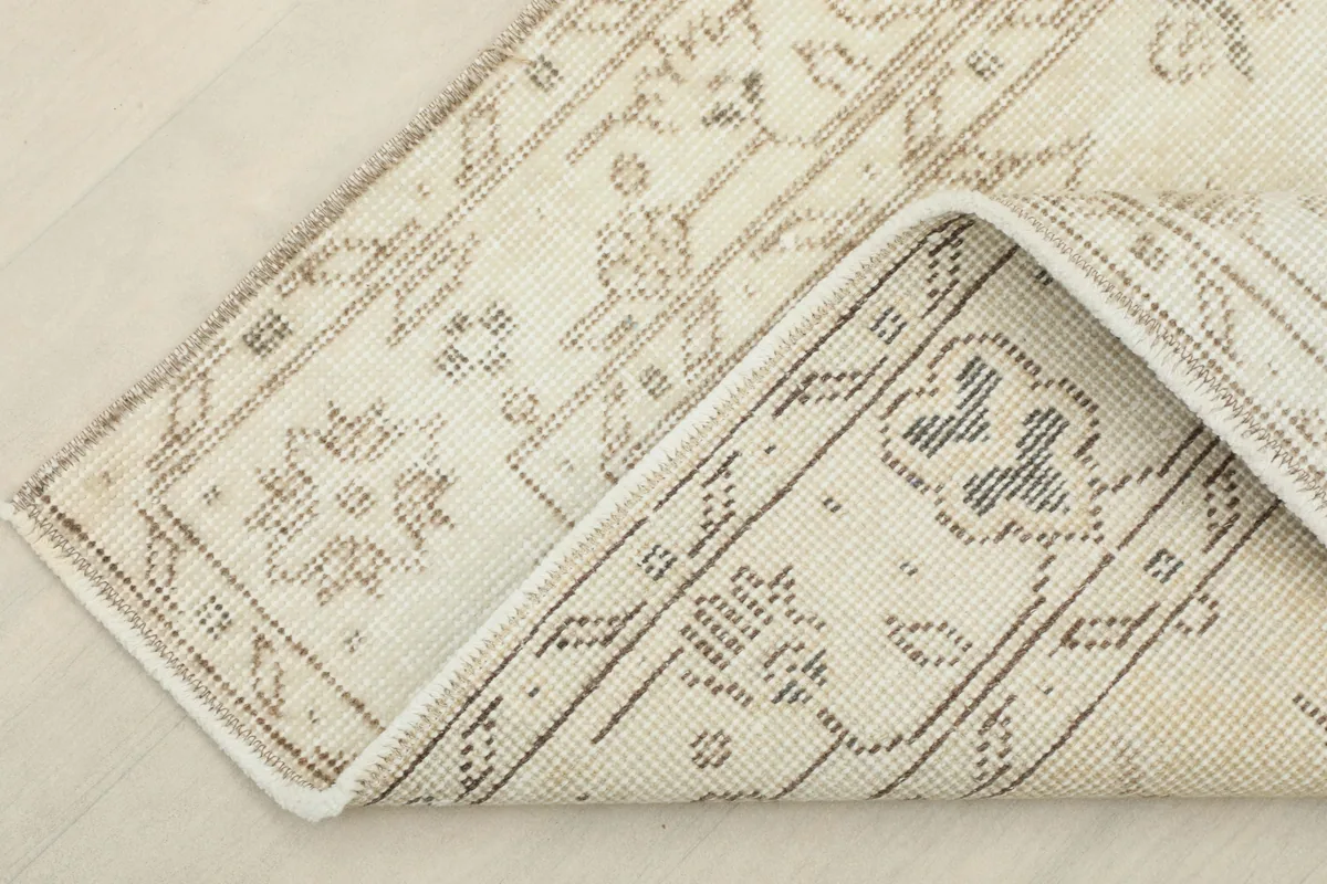 View showing the underside and a corner of the Beige Subtle Floral Rug, revealing the cotton foundation.