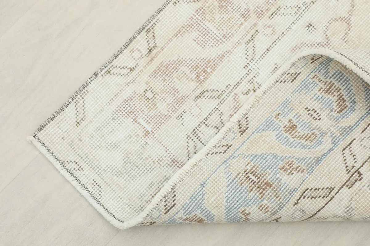 Corner of the rug folded back, revealing the cotton foundation and reverse side of the knots.